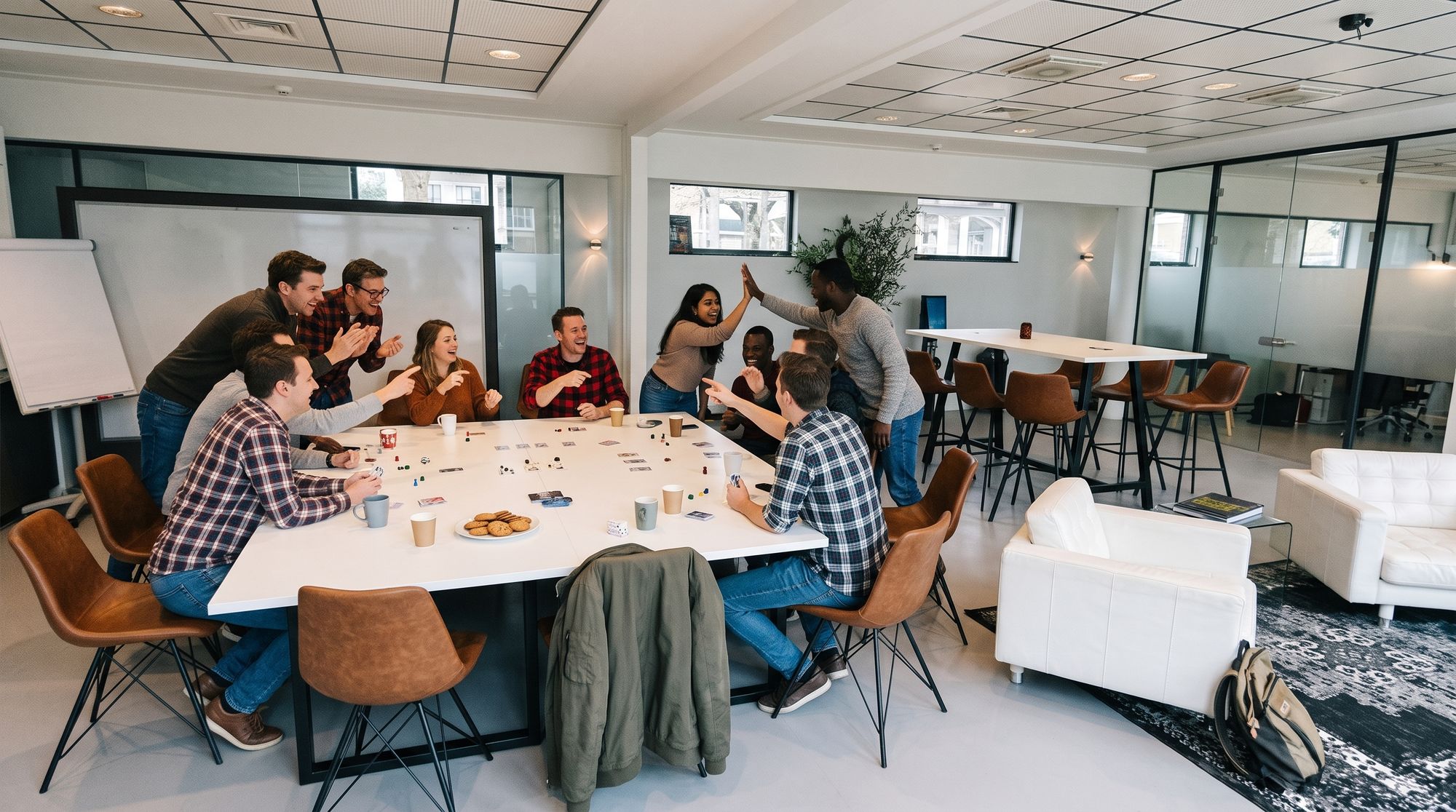 Collega's spelen lachend een spel aan de grote witte tafel bij Third Place en geven elkaar een high five
